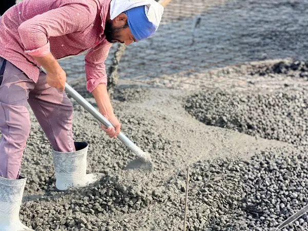Worker spreading wet concrete over a bed of aggregate with a shovel