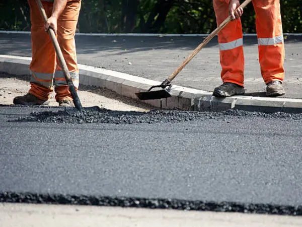 Two workers in hi-vis trousers spreading fresh asphalt along a kerb